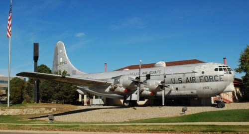 A vintage U.S. Air Force aircraft displayed outdoors, with a flag and building in the background.