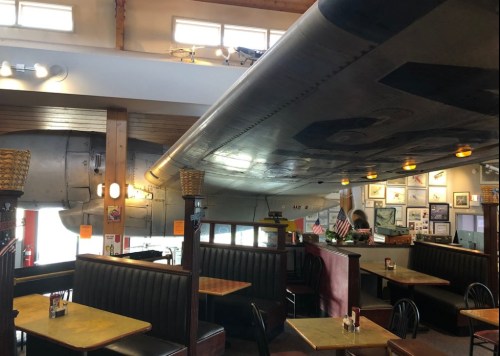 Interior of a restaurant featuring a large airplane wing overhead, with booths and decor reflecting aviation themes.
