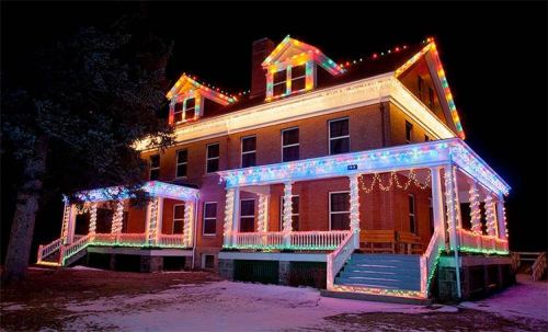 A large historic building decorated with colorful holiday lights at night, surrounded by snow.