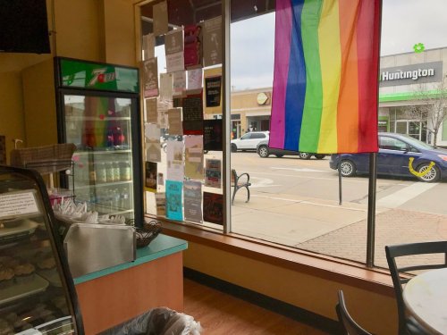 Interior of a café with a rainbow flag hanging in the window, showcasing a view of the street outside.
