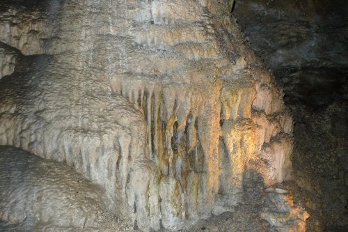 Stalactites and stalagmites in a dimly lit cave, showcasing textured rock formations and subtle lighting.