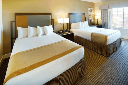 A hotel room featuring two beds with white linens, a nightstand, and a window with natural light.