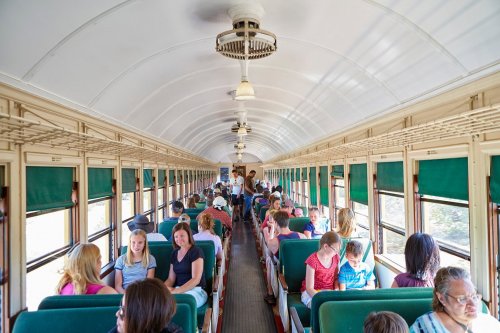 Interior of a vintage train car filled with passengers seated on both sides, enjoying the journey.