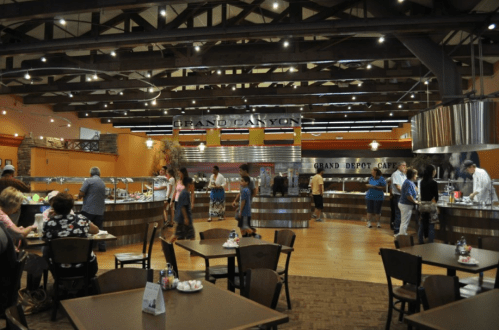 A bustling cafeteria with a large serving area, tables, and patrons enjoying meals in a warm, inviting atmosphere.