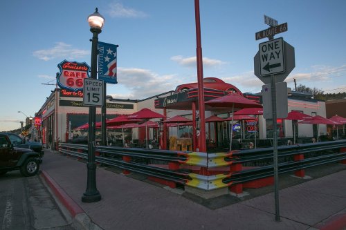 A retro diner on Route 66 with red umbrellas, a classic car on the roof, and vintage signage.