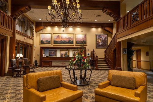 Cozy lobby with wooden accents, two yellow chairs, a floral arrangement, and a staircase leading to an upper level.