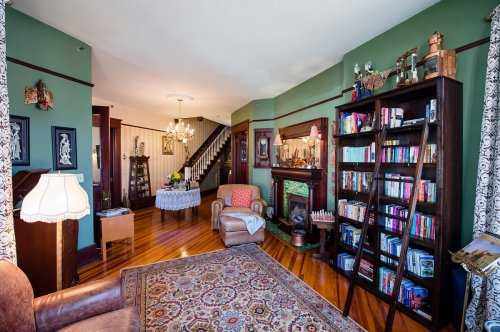 Cozy living room with green walls, a bookshelf, armchair, and a decorative rug, featuring a staircase in the background.