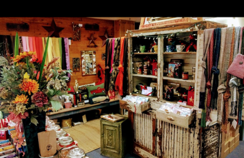 A cozy shop interior filled with colorful scarves, flowers, and vintage decor, featuring a rustic display cabinet.