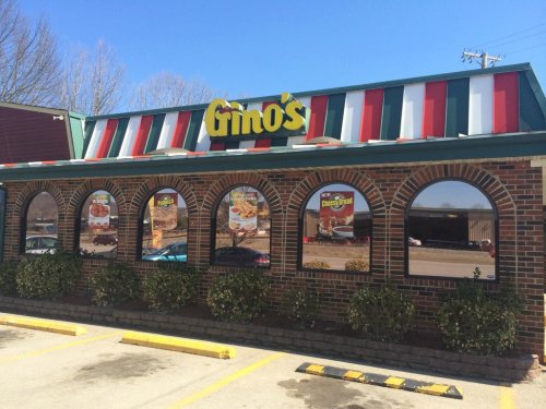 Exterior of Gino's restaurant featuring a colorful roof, brick facade, and large arched windows displaying menu items.