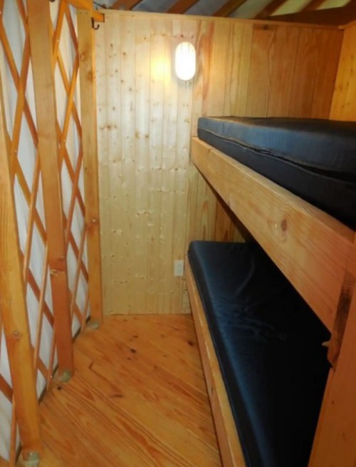 Interior of a wooden yurt with two bunk beds and warm lighting, featuring a cozy, rustic design.