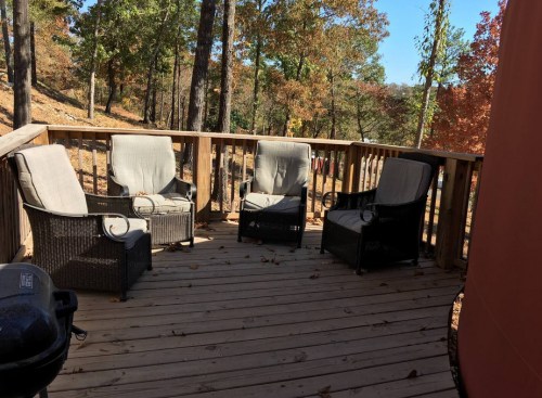 A wooden deck with four outdoor chairs surrounded by trees and autumn foliage.