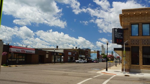 A street view featuring shops, a bank, and a clear blue sky with clouds. Temperature displayed at 83°F.