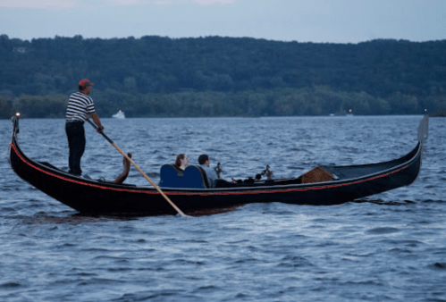 A gondola with a gondolier and passengers gliding across a calm lake at dusk.