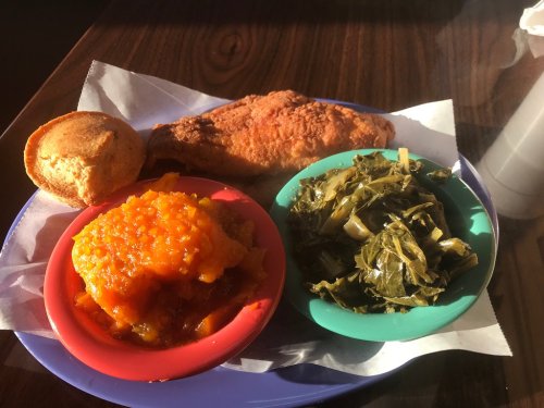 A plate featuring fried chicken, collard greens, sweet potato mash, and a cornbread muffin on a blue tray.