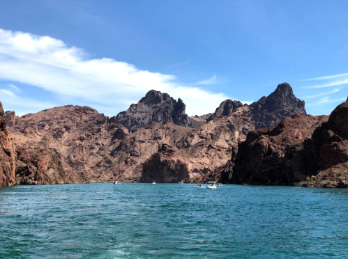 A serene lake surrounded by rugged, rocky mountains under a clear blue sky. Small boats are visible on the water.