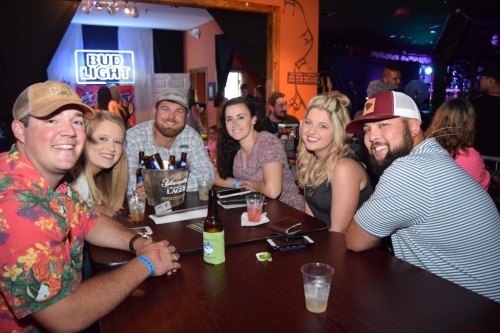 A group of six friends enjoying drinks at a lively bar, smiling and posing for the camera.