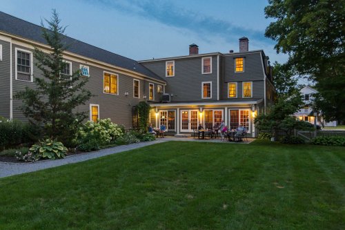 A cozy backyard view of a house at dusk, featuring a well-kept lawn and patio with people enjoying the evening.