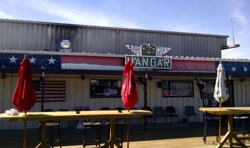 Exterior of a bar named "Hangar," featuring red umbrellas, American flags, and a patriotic color scheme.