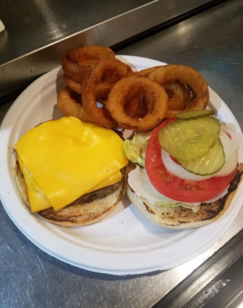 A plate with a cheeseburger topped with lettuce, tomato, pickles, and onion, alongside crispy onion rings.