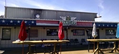 Exterior of a bar with patriotic decor, featuring umbrellas and a sign that reads "Hangar."