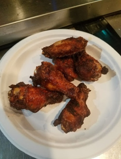 A plate of six crispy, golden-brown chicken wings arranged on a white paper plate.
