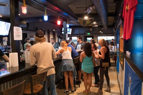 A lively bar scene with patrons socializing, ordering drinks, and enjoying the atmosphere under colorful lights.