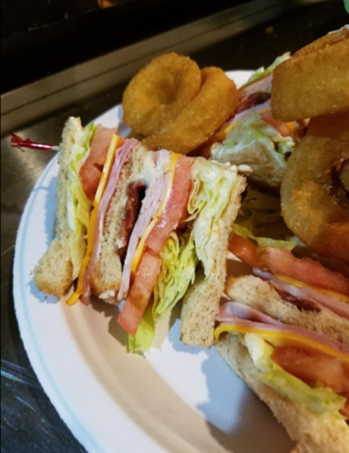 A plate with a layered sandwich featuring lettuce, tomato, and cheese, alongside onion rings.