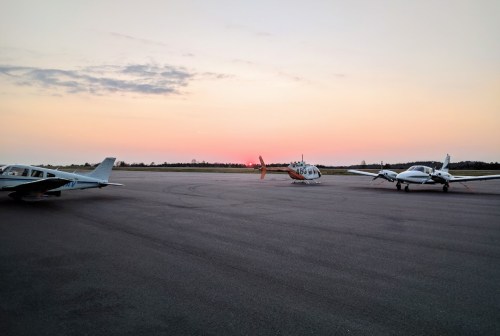 Three small aircraft parked on an airstrip at sunset, with a colorful sky in the background.