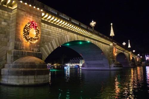 A beautifully lit bridge at night, adorned with festive decorations and reflections in the water below.