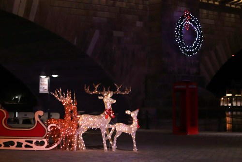 A festive display featuring illuminated reindeer, a sleigh, and a wreath, set against a dark background.
