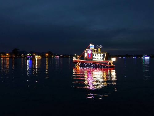A brightly lit boat decorated with colorful lights floats on calm water at night, reflecting its glow.