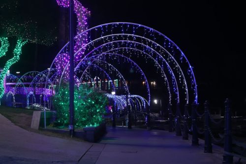 A pathway adorned with colorful purple and green holiday lights, creating a festive archway at night.