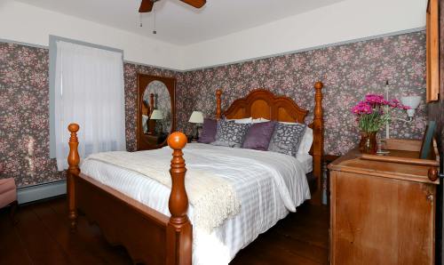 Cozy bedroom with floral wallpaper, a wooden bed, and a dresser, featuring a mirror and fresh flowers on a nightstand.