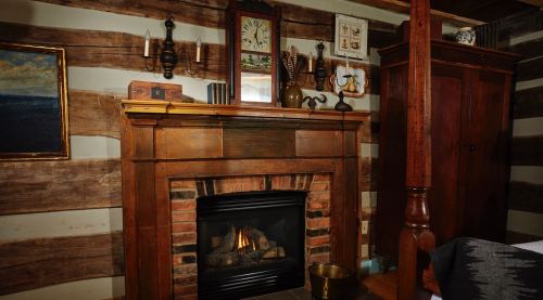 Cozy fireplace with a wooden mantel, surrounded by rustic decor in a log cabin setting.