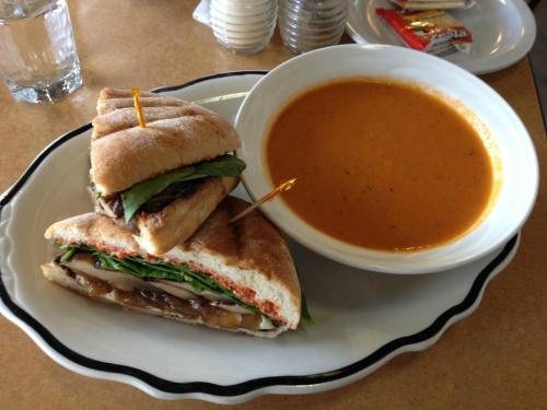 A plate with a sandwich filled with vegetables and a bowl of orange soup, garnished with toothpicks.