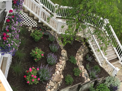Aerial view of a landscaped garden with colorful flowers, stone pathways, and a wooden staircase in the background.