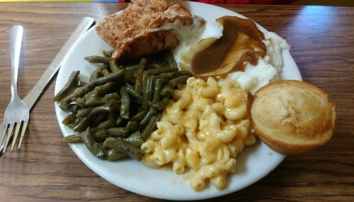 A plate of food featuring fried chicken, mashed potatoes with gravy, green beans, macaroni and cheese, and a cornbread muffin.