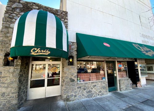 Exterior of a restaurant with a green and white striped awning, stone facade, and large glass windows.