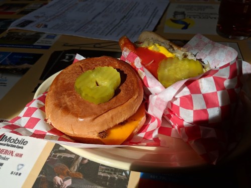 A plate with two sandwiches: one with cheese and pickles, the other with sausage, cheese, and ketchup, all in checkered wrappers.