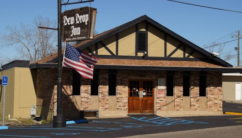 Exterior of the Dew Drop Inn, featuring a stone facade, a sign, and an American flag in front.