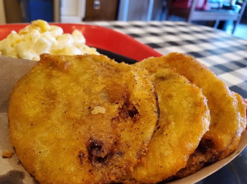 Three golden, crispy fried plantains served with a side of creamy macaroni and cheese on a checkered tablecloth.
