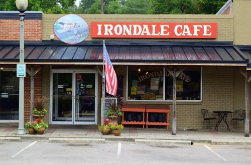 Exterior of Irondale Cafe featuring a sign, American flag, and potted plants on a sunny day.
