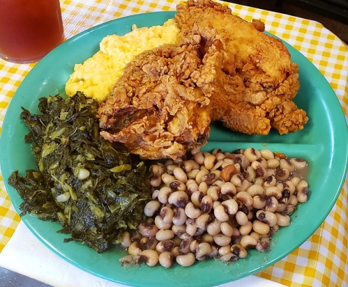 A green plate with fried chicken, collard greens, black-eyed peas, and creamy yellow grits.