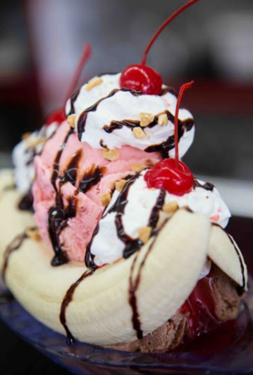 A banana split topped with scoops of pink and brown ice cream, whipped cream, chocolate syrup, and cherries.