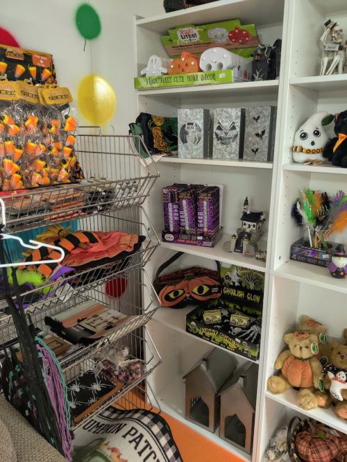A shelf filled with Halloween decorations, candy, and themed items, alongside a rack of colorful costumes and accessories.