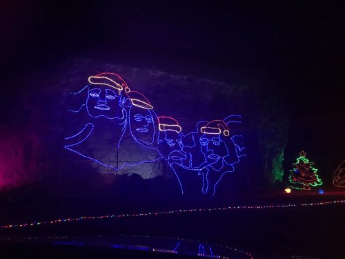 Colorful holiday lights depicting four figures wearing Santa hats, set against a dark background with a Christmas tree.