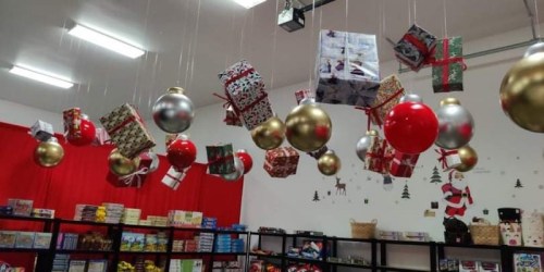 Colorful Christmas decorations, including hanging gifts and ornaments, in a festive store setting with a red backdrop.