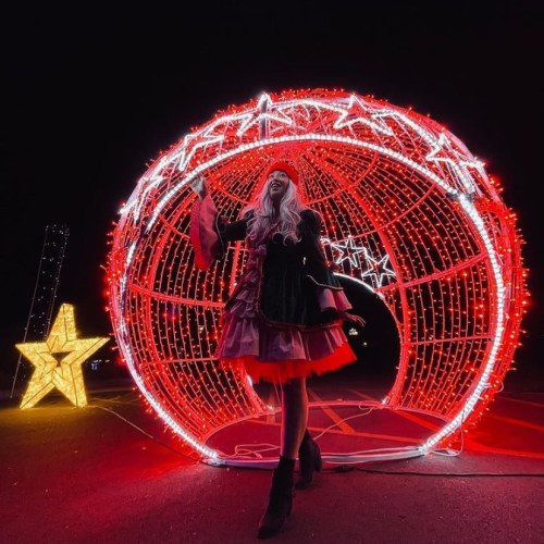 A person in a festive outfit stands inside a large illuminated red and white star-shaped display at night.