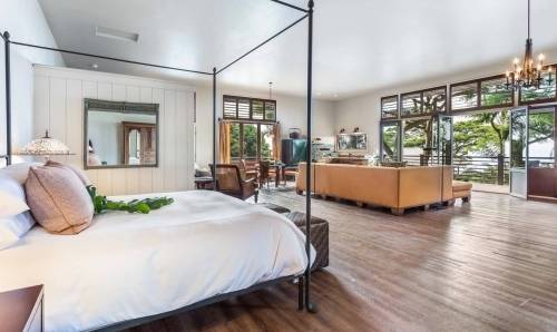 Spacious bedroom with a four-poster bed, wooden floors, and large windows overlooking a lush outdoor area.