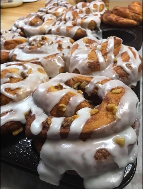 Freshly baked cinnamon rolls drizzled with white icing and topped with chopped nuts, arranged in a baking tray.